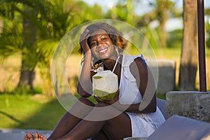 Young happy and attractive black afro American woman lying on pool hammock at tropical beach resort chilling relaxed drinking