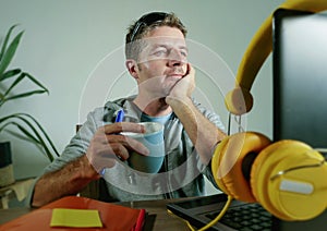 Young happy and attractive business man at home office drinking coffee cup looking satisfied and confident working with laptop com