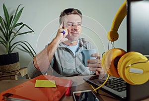 Young happy and attractive business man at home office drinking coffee cup looking satisfied and confident working with laptop com
