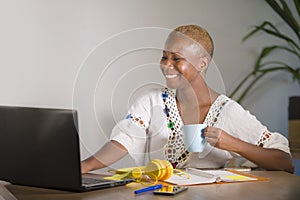 Young happy and attractive hipster black afro American woman drinking tea or coffee at home office working cheerful with laptop co