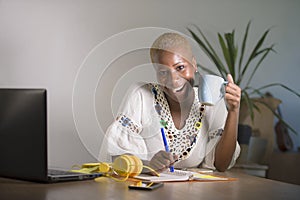 Young happy and attractive hipster black afro American woman drinking tea or coffee at home office working cheerful with laptop co