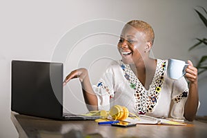 Young happy and attractive hipster black afro American woman drinking tea or coffee at home office working cheerful with laptop co