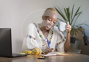 Young happy and attractive hipster black afro American woman drinking tea or coffee at home office working cheerful with laptop co