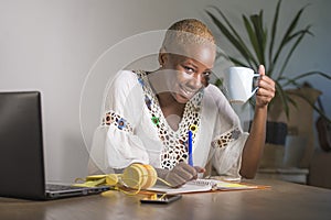 Young happy and attractive hipster black afro American woman drinking tea or coffee at home office working cheerful with laptop co