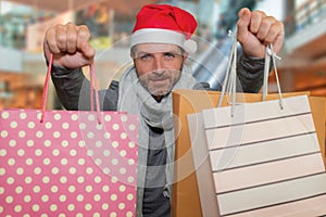 Young happy and attractive hipster man in Santa hat and scarf smiling holding lot of shopping bags buying Christmas presents