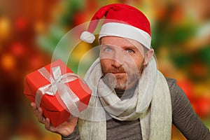 Young happy and attractive man in santa hat and scarf smiling holding Christmas gift box receiving or giving present isolated on