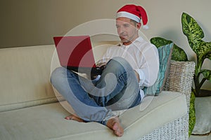 Young happy and attractive man in Santa Klaus hat using credit card and laptop computer for buying online Christmas presents and g