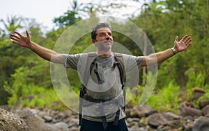 Young happy and attractive man with travel backpack hiking in river at forest feeling free enjoying nature and fresh environment