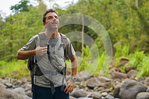 Young happy and attractive man with travel backpack hiking in river at forest feeling free enjoying nature and fresh environment