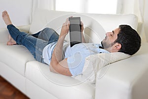 Young happy attractive man using digital pad or tablet sitting on couch