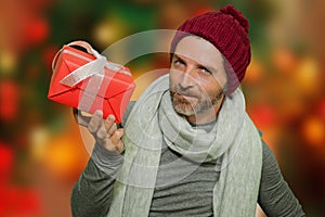 Young happy and attractive man in winter hat and scarf smiling holding Christmas gift box receiving or giving present  on