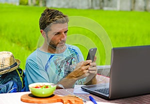 Young happy and attractive man working outdoors with laptop computer and mobile phone as internet travel blogger or digital nomad