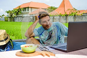 Young happy and attractive man working outdoors with laptop computer and mobile phone as internet travel blogger or digital nomad