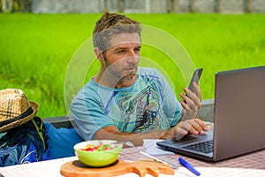 Young happy and attractive man working outdoors with laptop computer and mobile phone as internet travel blogger or digital nomad