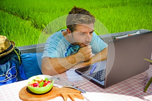 Young happy and attractive man working outdoors with laptop computer and mobile phone as internet travel blogger or digital nomad