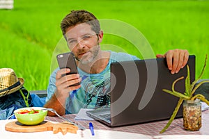 Young happy and attractive man working outdoors with laptop computer and mobile phone as internet travel blogger or digital nomad