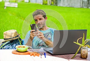 Young happy and attractive man working outdoors with laptop computer and mobile phone as internet travel blogger or digital nomad