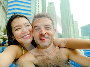 Young happy and attractive playful couple taking selfie picture together with mobile phone at luxury urban hotel infinity pool enj