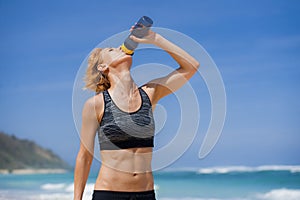 Young happy and attractive sport runner woman drinking water bottle or isotonic drink after running workout at tropical paradise b