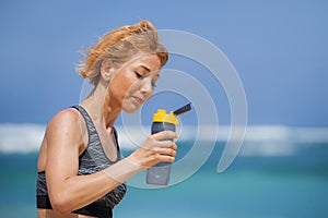 Young happy and attractive sport runner woman drinking water bottle or isotonic drink after running workout at tropical paradise b