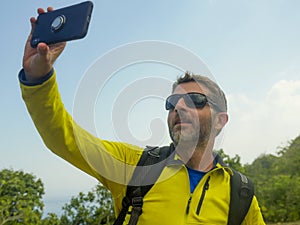 Young happy and attractive sporty hiker man with trekking backpack hiking at mountain taking selfie enjoying travel getaway