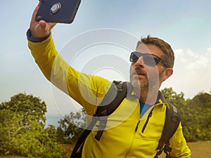 Young happy and attractive sporty hiker man with trekking backpack hiking at mountain taking selfie enjoying travel getaway