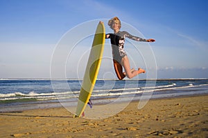 Young happy and attractive surfer girl jumping high in the air holding surf board before surfing at beautiful tropical beach enjoy