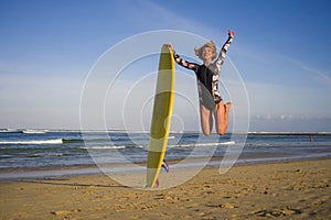 Young happy and attractive surfer girl jumping high in the air holding surf board before surfing at beautiful tropical beach enjoy