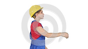 Young happy attractive woman in construction uniform putting yellow construction hat on while walking on white