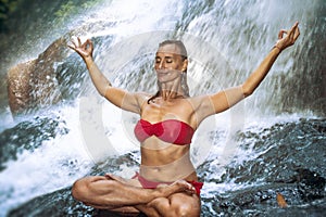 Young happy and attractive woman doing yoga exercise posing under beautiful tropical waterfall getting wet smiling happy in medita