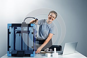 Young happy attractive woman entrepreneur fixing the tube on 3D printer to make prototype. Preparation for 3d printing