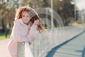 Young happy attractive woman posing on a fence near a running track