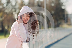 Young happy attractive woman posing on a fence near a running track