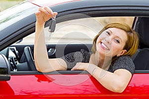 Young happy attractive woman smiling proud sitting at driver seat holding and showing car key in new automobile buy and rent conce