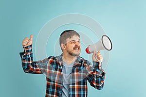 Young happy bearded man in casual clothes with megaphone isolated on light blue background.