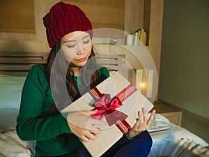 Young happy and beautiful Asian American girl in winter hat holding Christmas present box with ribbon smiling excited and cheerful