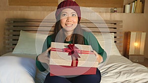 Young happy beautiful Asian American woman in winter hat holding Christmas giftbox with ribbon smiling excited and cheerful receiv