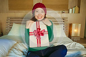 Young happy and beautiful Asian American woman in winter hat holding Christmas present box with ribbon smiling excited and cheerfu