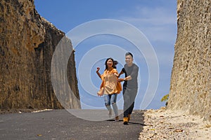 Young happy and beautiful Asian Chinese couple in love enjoying outdoors journey running playful in cliff rock road exploring the