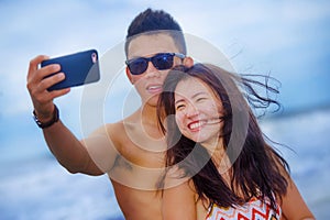 Young happy and beautiful Asian Chinese couple taking selfie photo with mobile phone camera smiling joyful