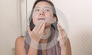 Young happy and beautiful Asian Chinese woman applying moisturizer facial cream and beauty treatment at home bathroom in morning