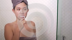 Young happy and beautiful Asian Chinese woman brushing her teeth wearing head towel wrap at bathroom mirror