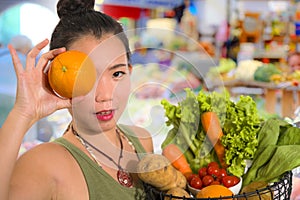 Young happy and beautiful Asian Chinese woman holding basket full of fresh vegetables and fruits smiling cheerful buying healthy