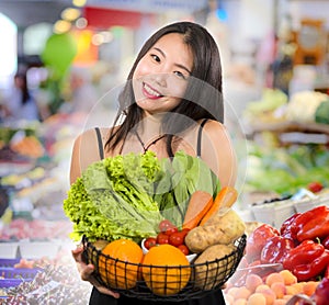 Young happy and beautiful Asian Chinese woman holding basket full of fresh vegetables and fruits smiling cheerful buying healthy