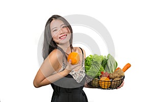 Young happy and beautiful Asian Chinese woman holding basket full of vegetables smiling cheerful holding orange playful in healthy