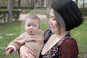 young happy and beautiful Asian Chinese woman holding little daughter, a cute an adorable baby girl, playful together in the park