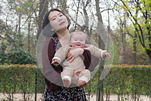 young happy and beautiful Asian Chinese woman holding little daughter, a cute an adorable baby girl, playful together in the park