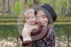 young happy and beautiful Asian Chinese woman holding little daughter, a cute an adorable baby girl, playful together in the park