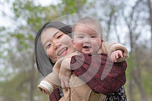young happy and beautiful Asian Chinese woman holding little daughter, a cute an adorable baby girl, playful together in the park