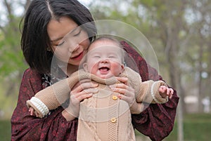 young happy and beautiful Asian Chinese woman holding little daughter, a cute an adorable baby girl, playful together in the park